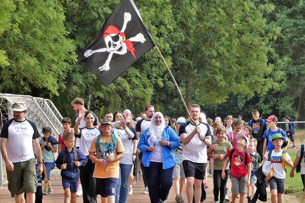 Städtische Ferienspiele unter dem Motto »Ferienspiele Dietzenbach Ahoi - Piraten auf Schatzsuche« gestartet. Das Bild zeigt eine Gruppe von Betreuern und Kindern mit einer großen Piratenflagge im Dietzenbacher Waldstadion.