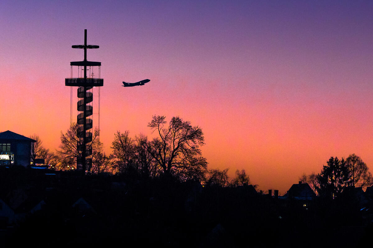 Bild vergrößern: Blick am Abend auf den Aussichtsturm mit vorbeifliegendem Flugzeug.