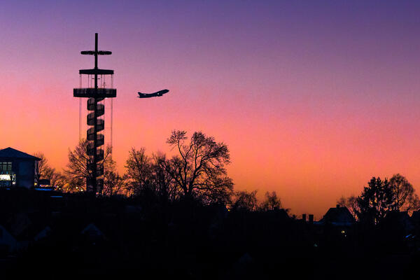Blick am Abend auf den Aussichtsturm mit vorbeifliegendem Flugzeug.