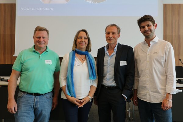 Vier Personen, drei M&auml;nner und eine Frau, stehen in einem Konferenzsaal.