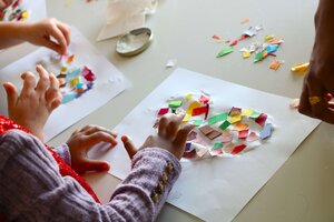 Bild vergr&ouml;&szlig;ern: Kinderh&auml;nde, die bunte Papierschnipsel in Herzform kleben.
