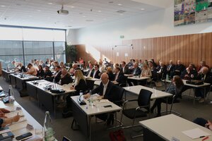 Bild vergr&ouml;&szlig;ern: Frauen und M&auml;nner an Tischen sitzend in einem Konferenzsaal
