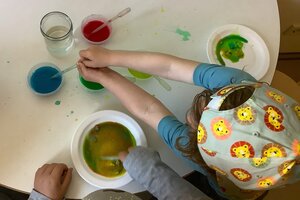 Bild vergr&ouml;&szlig;ern: Kinder sitzen vor Malfarben und Wassert&ouml;pfen und r&uuml;hren darin.