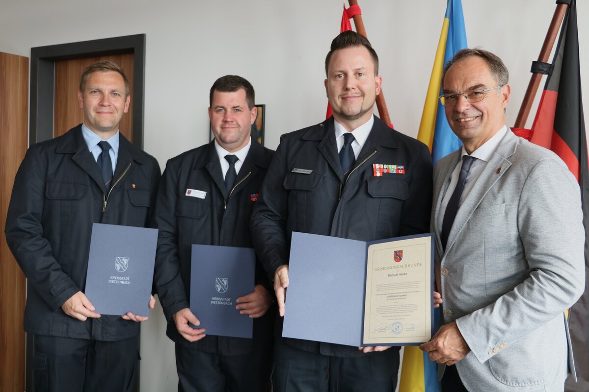 Vier M&auml;nner, davon drei in Uniform, die eine Urkunde halten.
