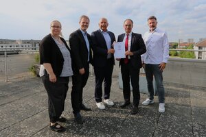 Bild vergr&ouml;&szlig;ern: Vier M&auml;nner und eine Frau stehen zusammen, unter ihnen der B&uuml;rgermeister von Dietzenbach und Hessens Innenminister Roman Poseck. Diese beiden halten eine Urkunde mit aufgedrucktem Wappen in den H&auml;nden.