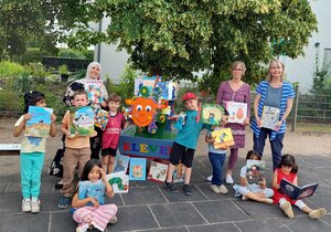 Bild vergr&ouml;&szlig;ern: Das bunte B&uuml;cherschaf &raquo;Eleven&laquo; der Kita 11 reist seit mehr als zwei Jahren durch die Kreisstadt Dietzenbach - jetzt auch stabil aus Holz und mit eigenem Wagen. Im Bild: Begeisterte Kinder mit Kita-11-Leiterin Kathrin Lyrhammer und Astrid Spina, Fachkraft f&uuml;r Sprachf&ouml;rderung (rechts).