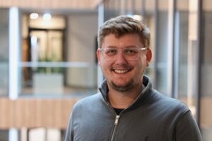 Bild vergr&ouml;&szlig;ern: Ein junger Mann mit Brille, er l&auml;chelt in die Kamera.