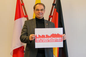 Bild vergrößern: Bürgermeister Dr. Dieter Lang mit einem Schild, das die Aufschrift "Aktionsbündnis Für die Würde unserer Städte" trägt.